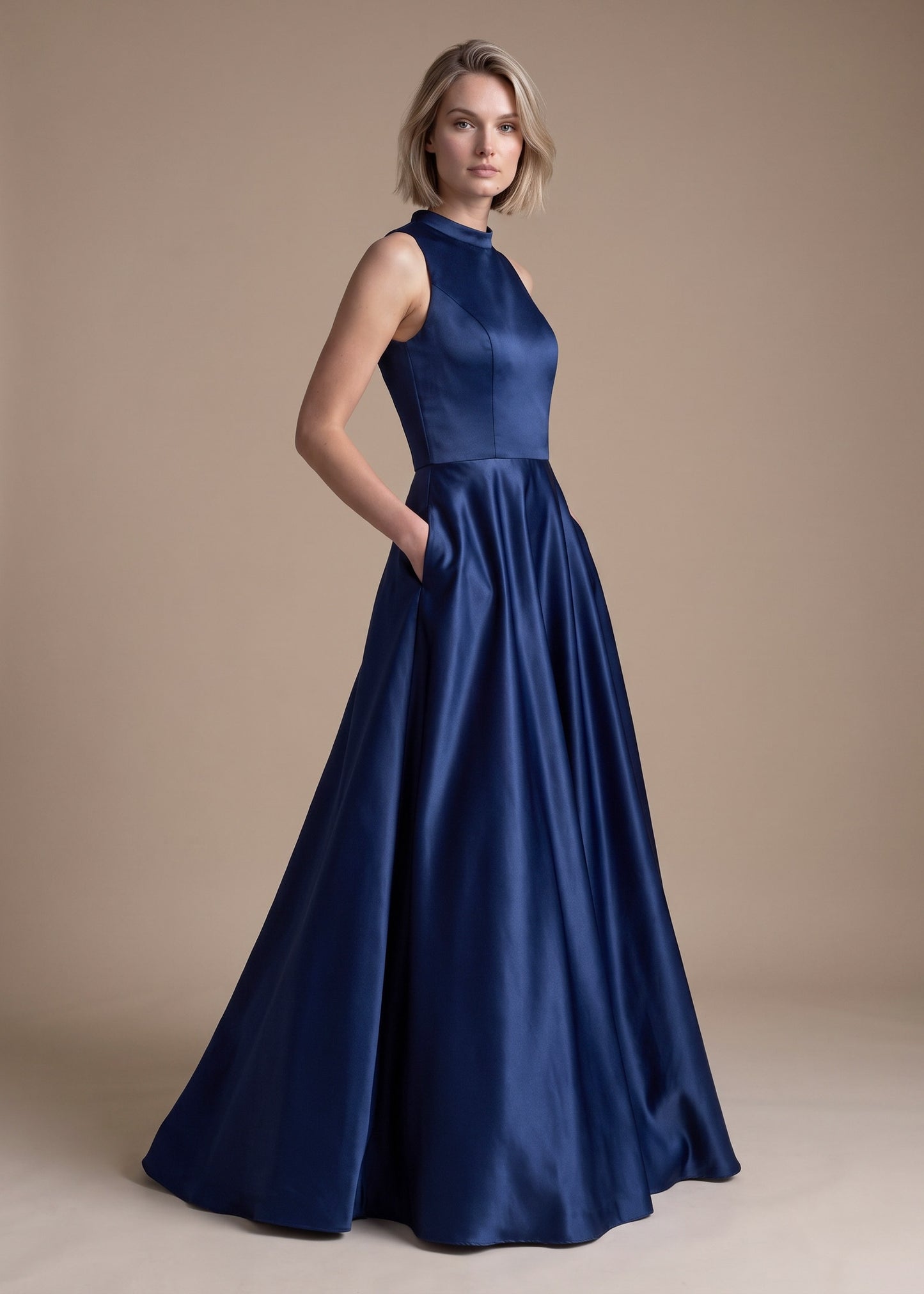 A woman modeling a sleeveless navy blue satin formal gown with a high neckline and a full, flowing skirt against a plain beige studio backdrop.